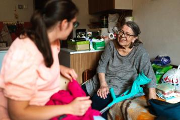 A caregiver helps a senior woman with a crutch