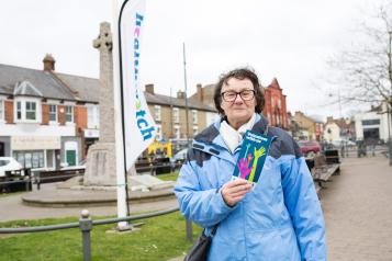 Healthwatch volunteer holding a leaflet on volunteering and stood in front of a Healthwatch banner