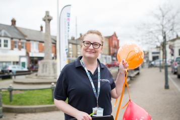 Healthwatch volunteer stood outside holding balloons