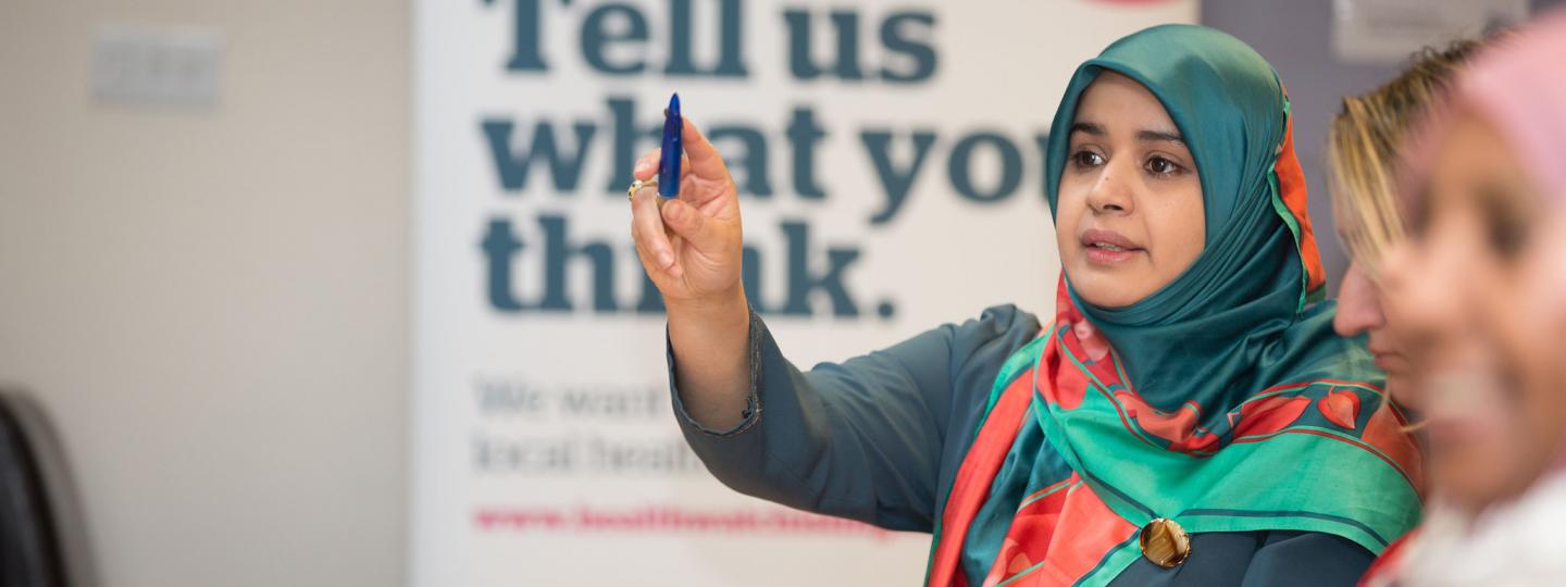 Woman in headscarf putting her hand up at Healthwatch event