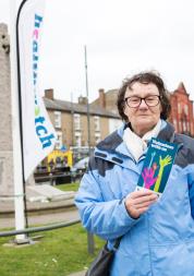 Healthwatch volunteer holding a leaflet on volunteering and stood in front of a Healthwatch banner